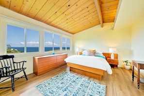 Une chambre avec un plafond en bois, un grand lit, une table de chevet, une commode, une chaise et une vue sur la mer.