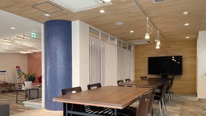 Een moderne vergaderruimte met een houten tafel, zwarte stoelen en een grote flatscreen-televisie.