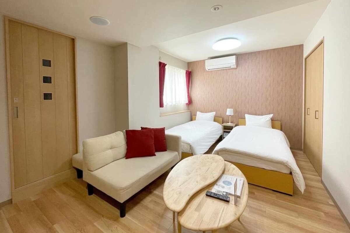 Une chambre d’hôtel avec un canapé, deux lits simples, une petite table, un appareil de climatisation et une armoire en bois.