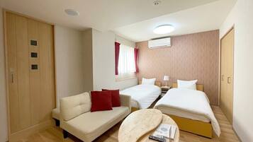 Ein Hotelzimmer mit einer Couch, zwei Einzelbetten, einem kleinen Tisch, einer Klimaanlage und einem Holzschrank.