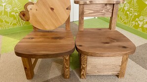 Twee houten stoelen met een uniek ontwerp, geplaatst op een vloerbedekking met een groene en witte behangachtergrond.