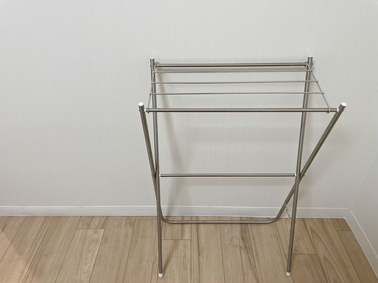 Ein Wäscheständer aus Metall mit drei horizontalen Stangen vor einer schlichten Wand und Holzboden.