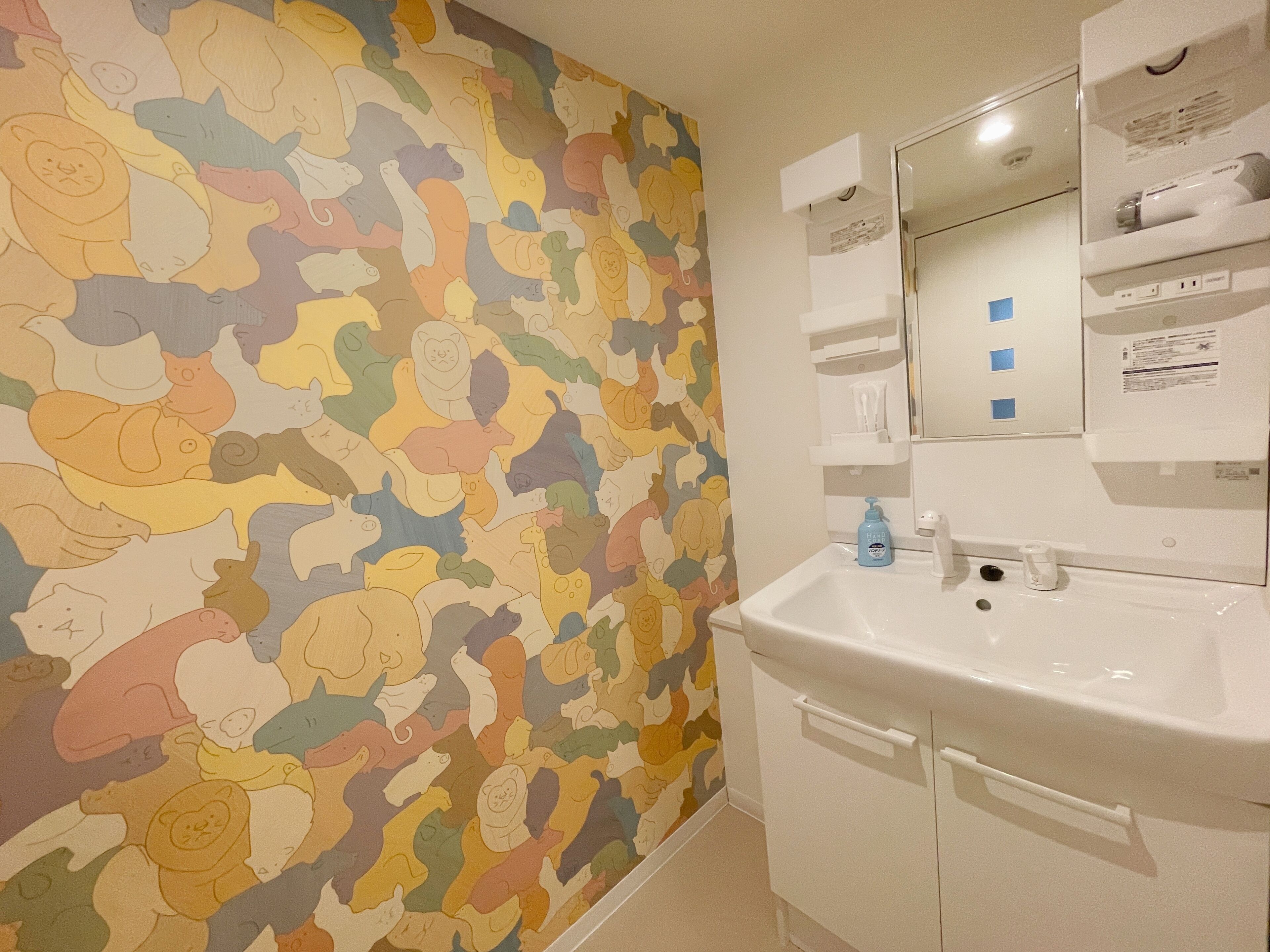 A bathroom with a colorful animal-themed wall, a white sink, and a mirror above it.