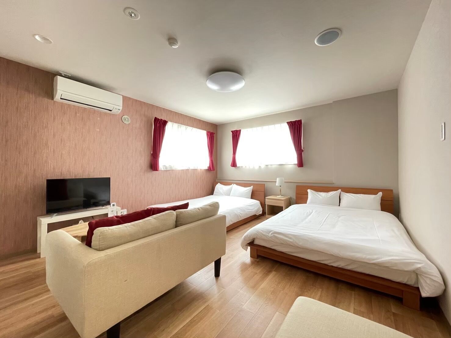 A modern hotel room with two single beds, a sofa, a TV, and a ceiling-mounted air conditioner.