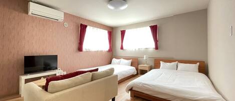 A modern hotel room with two single beds, a sofa, a TV, and a ceiling-mounted air conditioner.