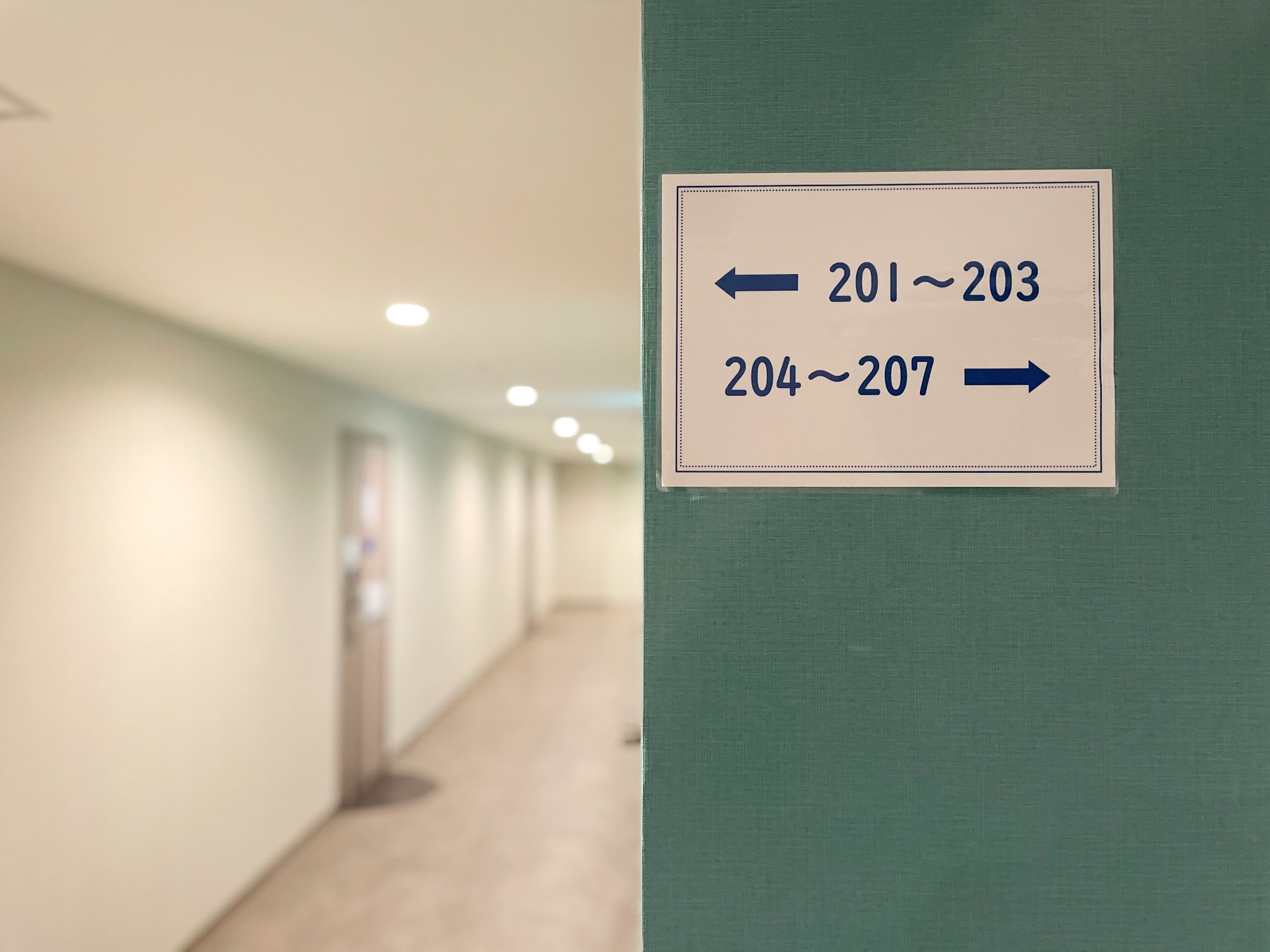 Een gang met richtingwijzers die kamernummers 201-203 aan de linkerkant en 204-207 aan de rechterkant aangeven.