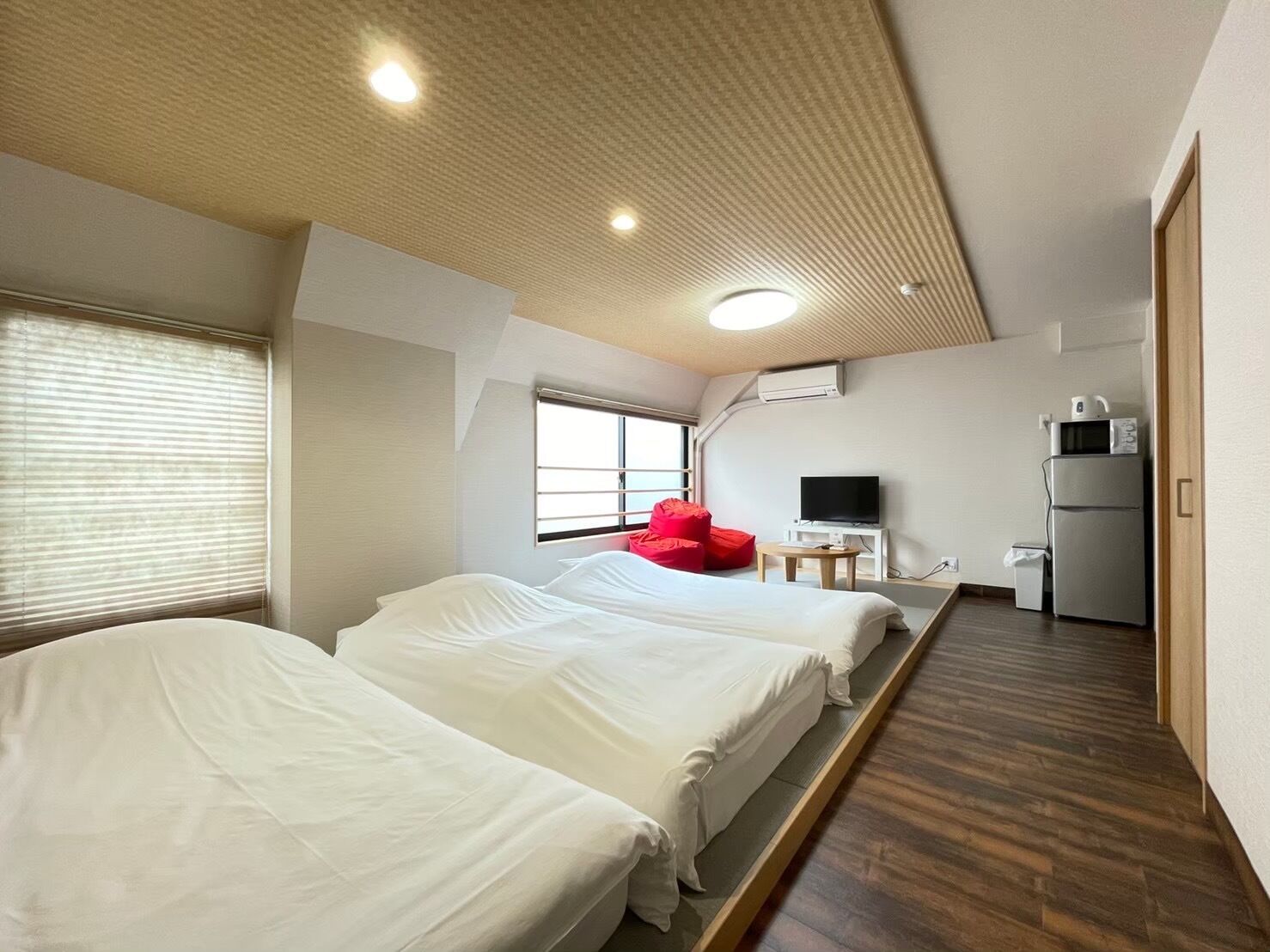 A hotel room with two beds, a TV, a refrigerator, and a small table.