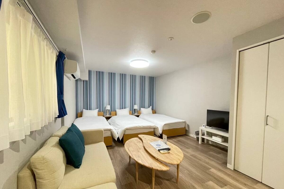 Une chambre d’hôtel avec deux lits simples, un canapé, une petite table, une télévision et une armoire.