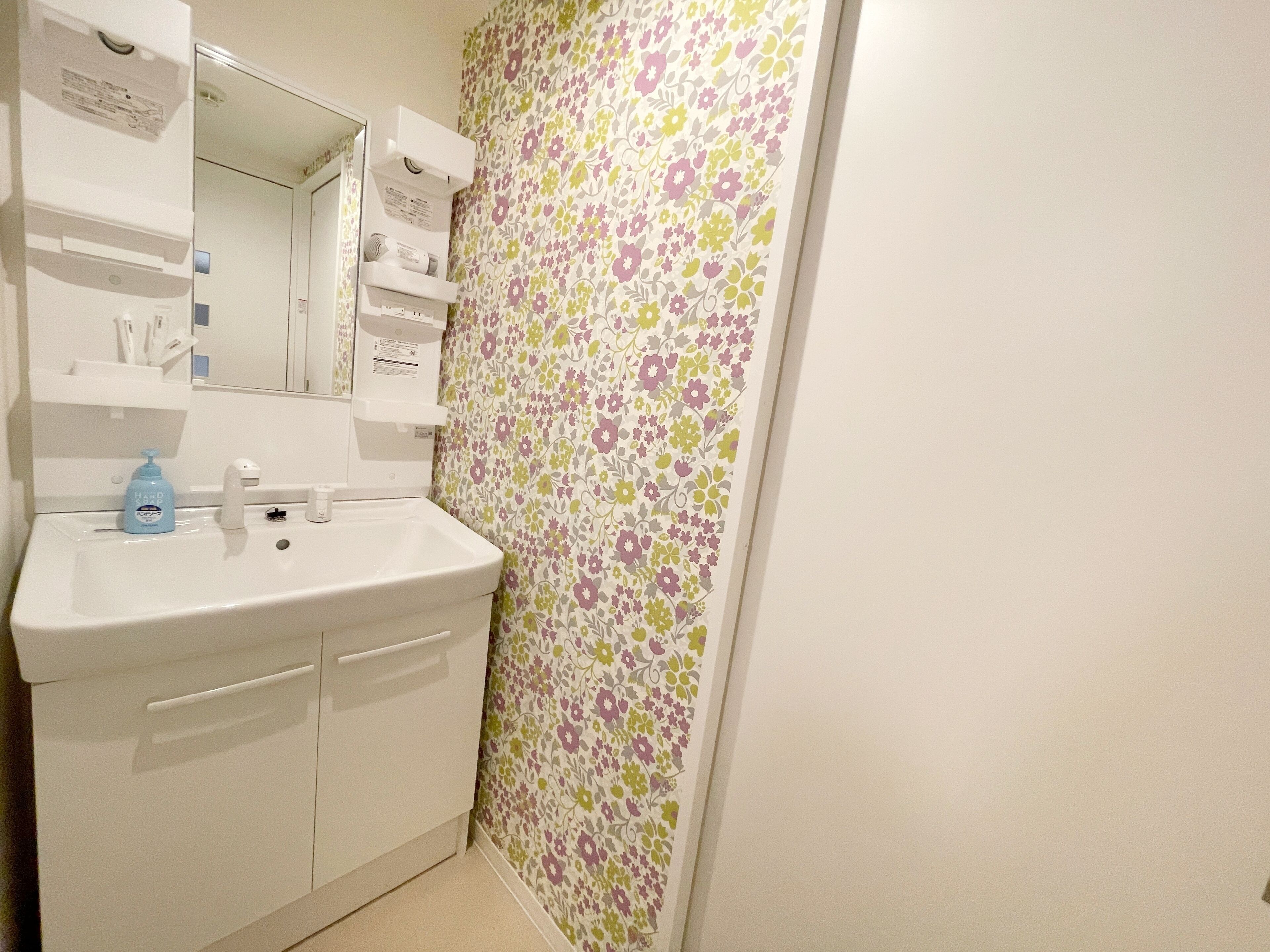 Casa de banho com lavatório, espelho e papel de parede floral.