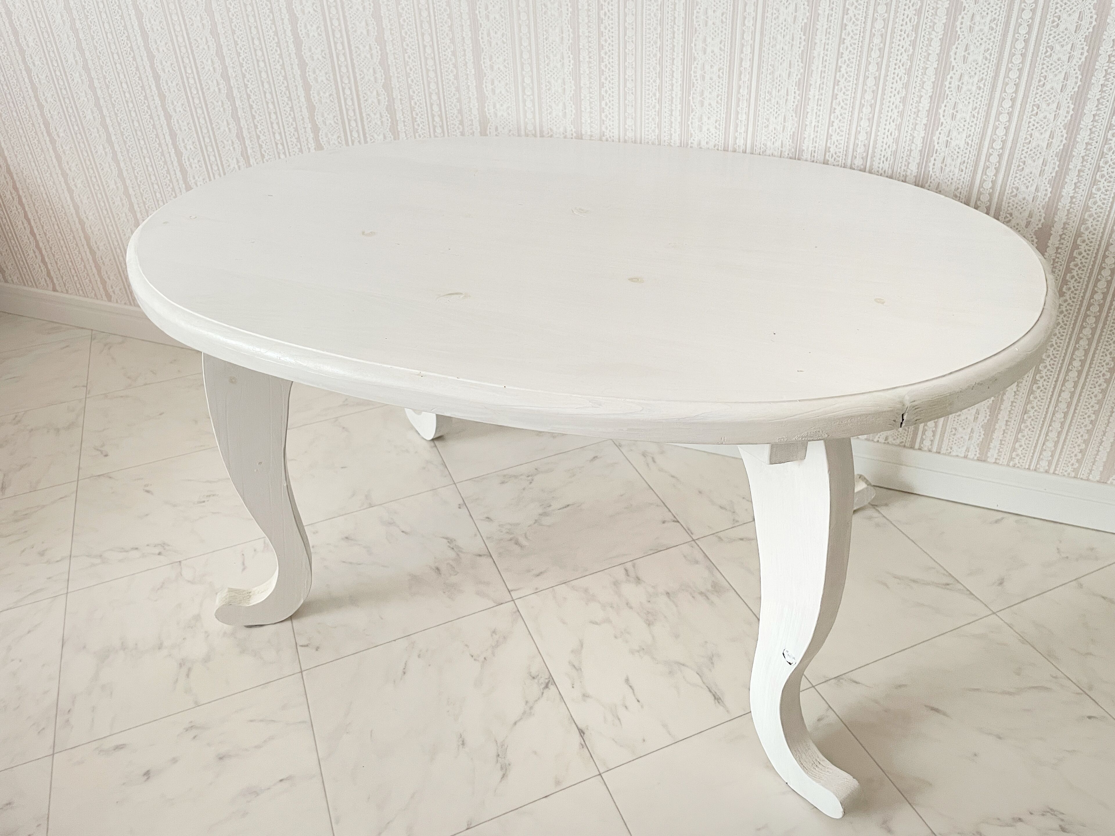 Una mesa blanca con patas curvas en una habitación con papel tapiz estampado y suelo de mármol.