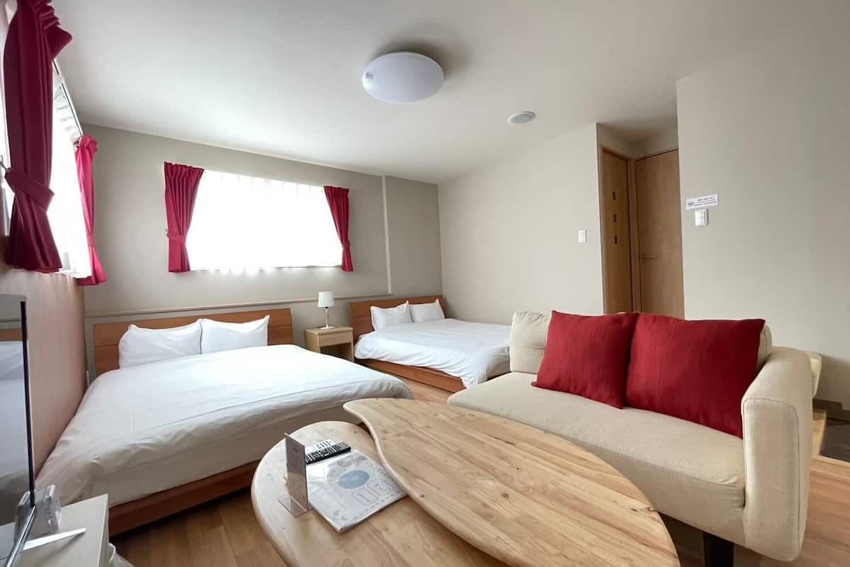 Une chambre d’hôtel avec deux lits, un canapé, une table en bois et une fenêtre avec des rideaux.