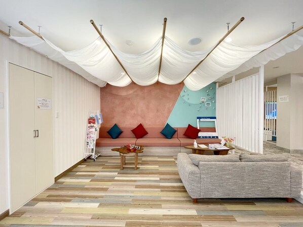 Un salon moderne avec un canapé, une table basse et un téléviseur fixé au mur. Le sol est en bois et le plafond est blanc, avec un tissu drapé.