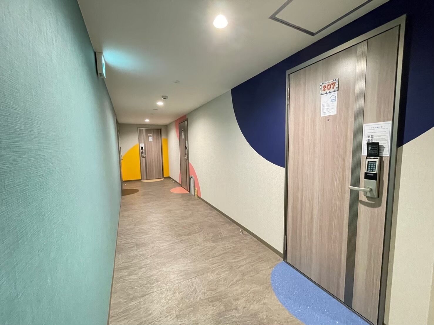 Un couloir doté d’un plancher en bois, d’un mur bleu et d’une porte équipée d’un système de verrouillage à clavier.
