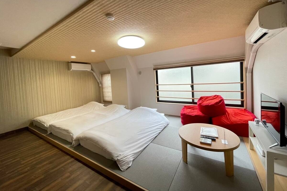 Une chambre d’hôtel moderne avec un grand lit, une petite table ronde, un téléviseur et un fauteuil rouge.
