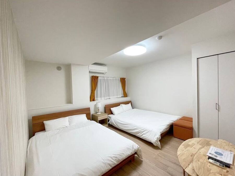 Quarto de hotel com duas camas de solteiro, piso de madeira, uma mesa redonda e um guarda-roupa.