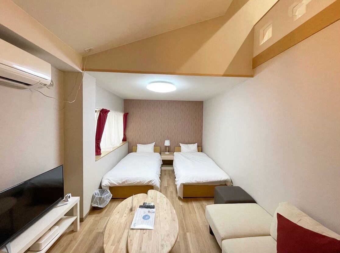 Ein kleines Hotelzimmer mit zwei Einzelbetten, einem Flachbildfernseher, einem kleinen runden Tisch und einer Couch.