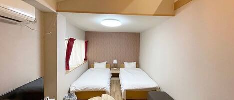 Ein kleines Hotelzimmer mit zwei Einzelbetten, einem Flachbildfernseher, einem kleinen runden Tisch und einer Couch.