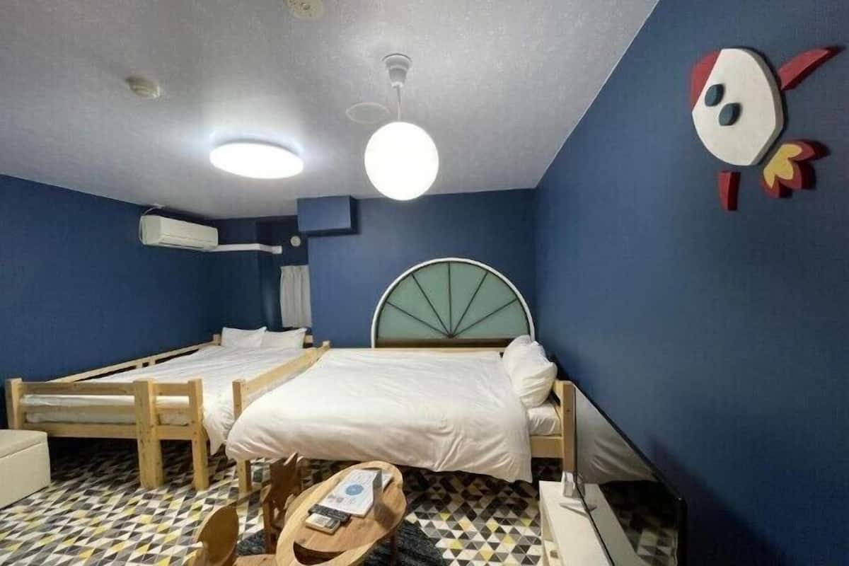 Une pièce avec deux lits, une table en bois, une chaise, une horloge murale et un ventilateur de plafond.