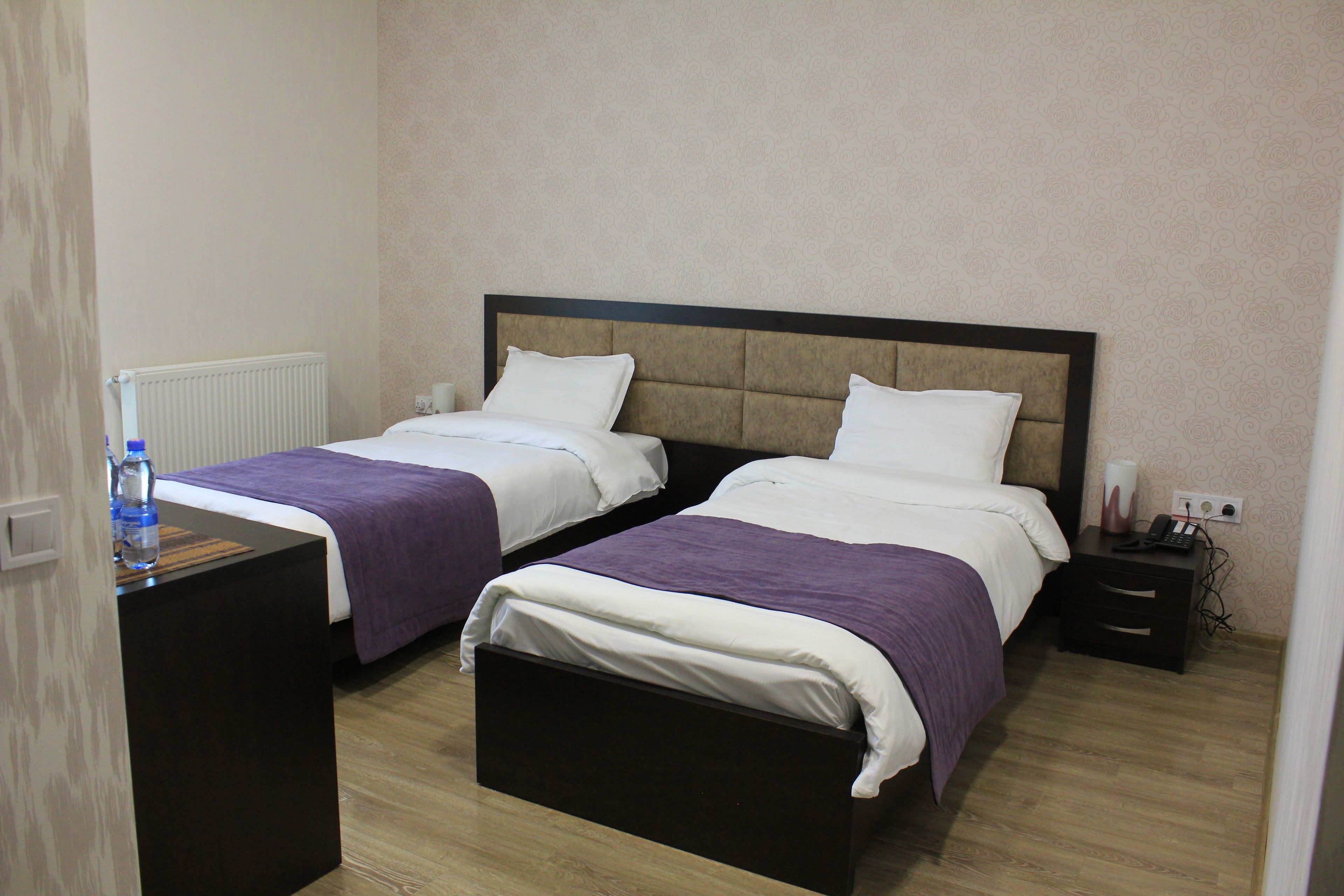 Ein Hotelzimmer mit zwei Betten, einem Nachttisch, einem Heizkörper und einem Beistelltisch.