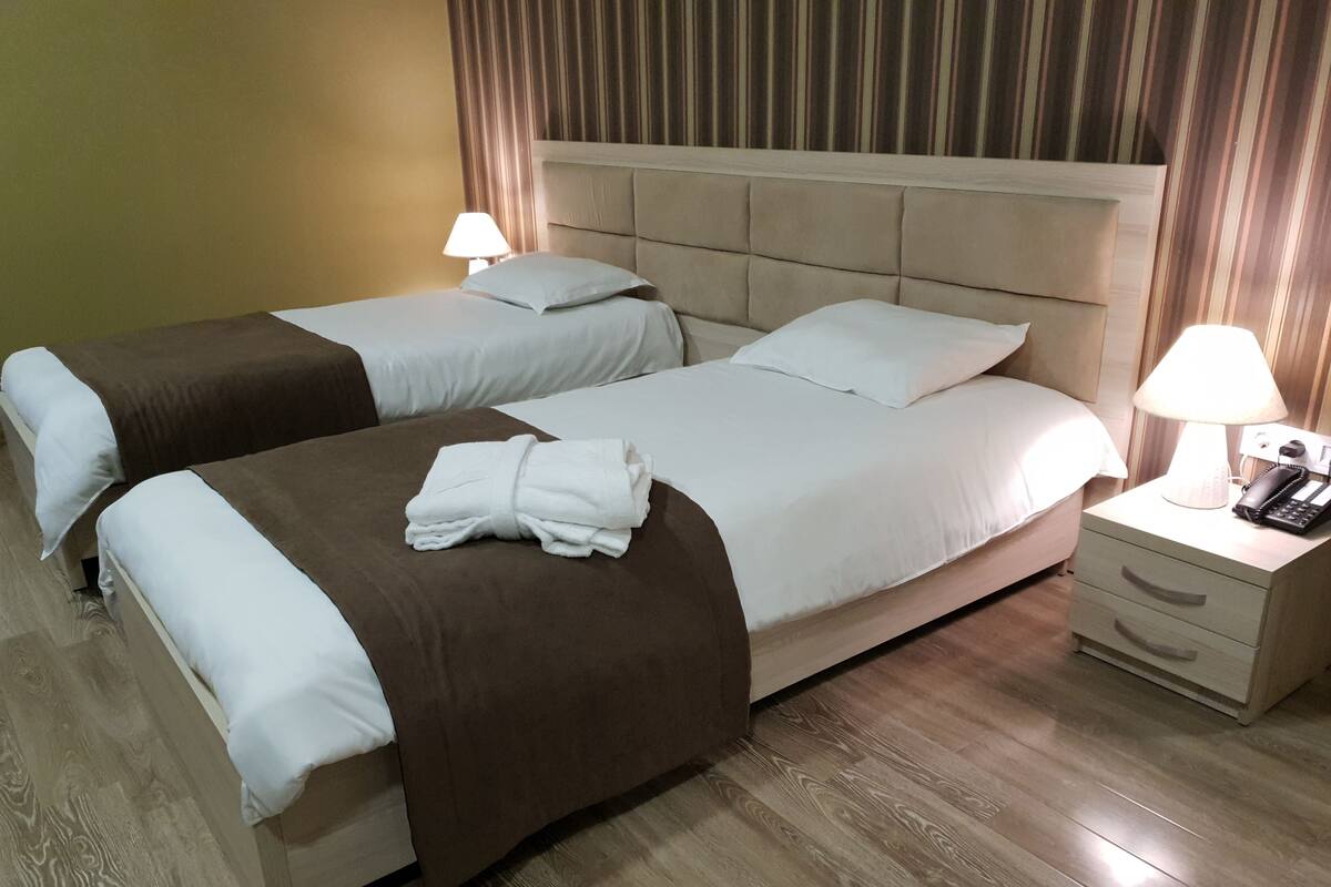 A hotel room with two beds, a nightstand with a lamp and phone, and a wooden floor.