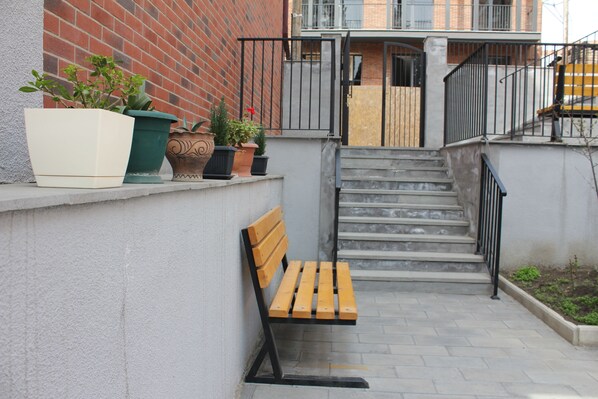 Eine Treppe führt zu einem Balkon, mit einer hölzernen Bank und Blumentöpfen auf einem Podest.