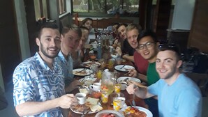 A group of people seated around a wooden table with various food items and drinks.