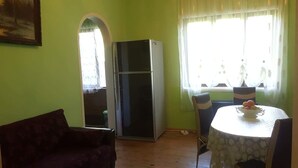 A room with a sofa, a table with a fruit bowl, a refrigerator, and a window with curtains. - beautiful sea garden (batumi)