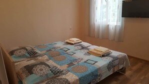 A single bed with a patterned bedspread and two pillows, a flat-screen TV mounted on the wall, and a window with sheer curtains. - beautiful sea garden (batumi)