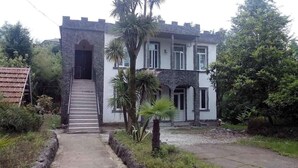 A two-story building with a stone facade, a staircase leading to the entrance, and a garden area with palm trees. - beautiful sea garden (batumi)