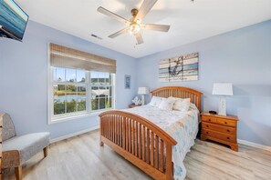 Quarto com cama, ventoinha no teto, janela com vista, mesa de cabeceira e uma cadeira.