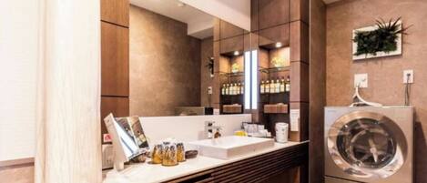 Un baño moderno con un espejo grande, muebles de madera, lavadora integrada y una encimera con artículos de aseo.
