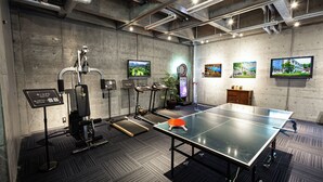A room with a ping pong table, exercise equipment, and multiple screens on the walls. - Hotel Pasela Living (Tokyo)
