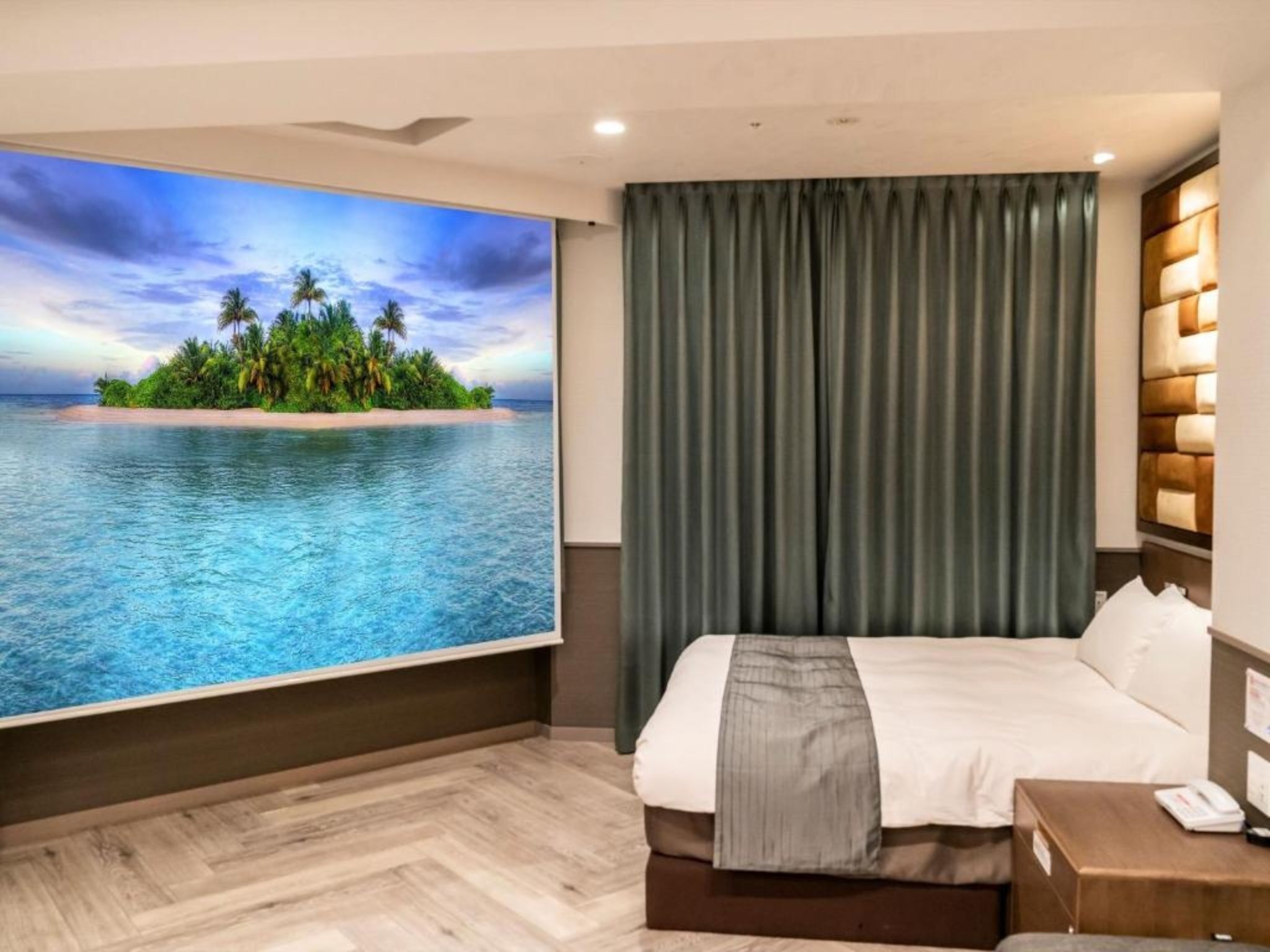 A hotel room with a bed, a nightstand, a telephone, and a large window with a tropical view.