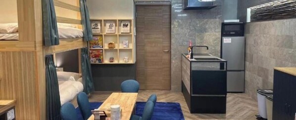 A compact hotel room with a bunk bed, a small kitchenette, a dining area with a table and chairs, and a bookshelf. - Hotel Pasela Living (Tokyo)
