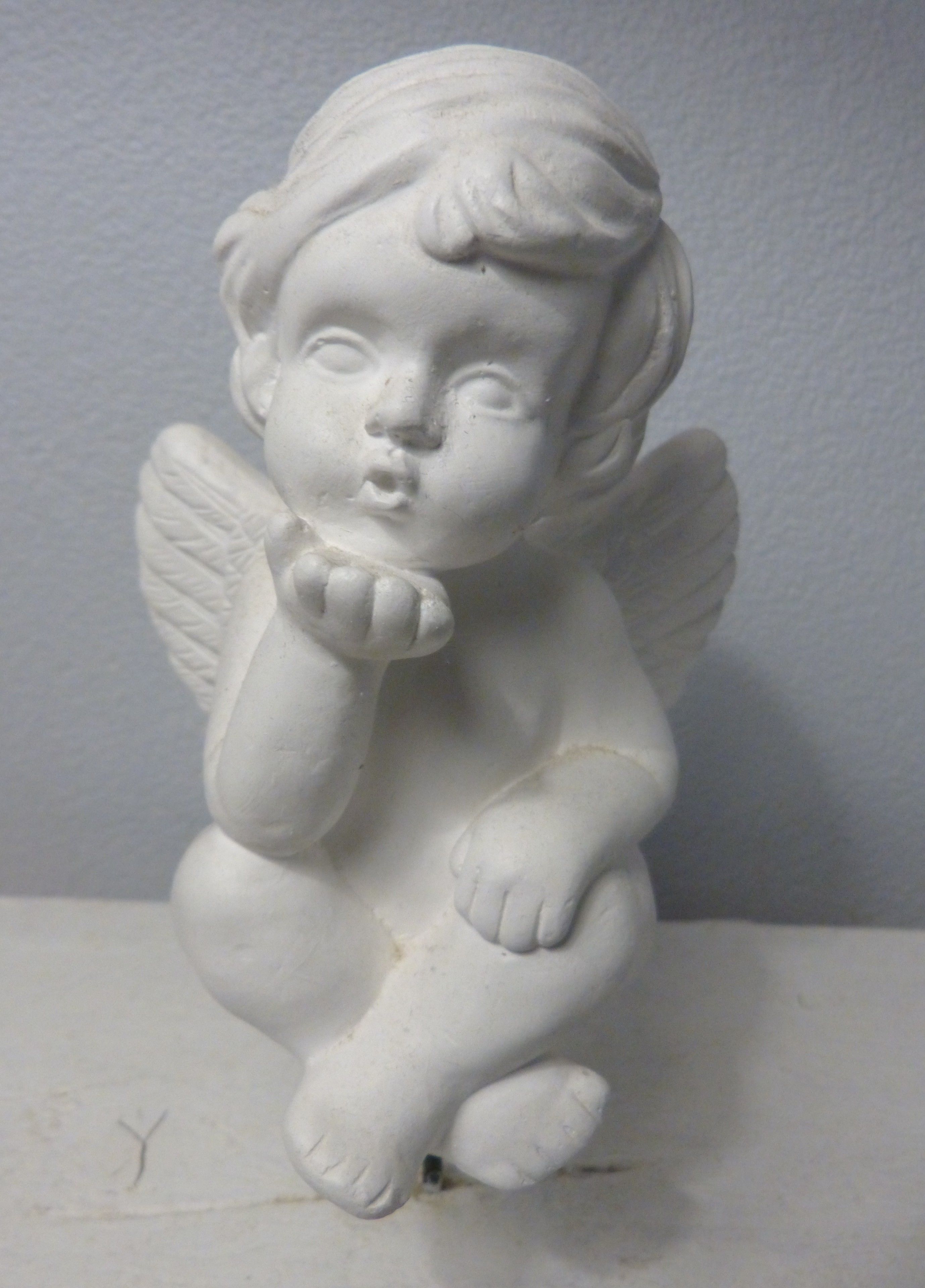 A white marble statue of a cherub with wings, positioned against a plain background.