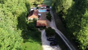 An aerial view of a property with a swimming pool, a red-roofed building, and a gravel driveway with two cars parked. - Chambres d'hôtes La Vergne (Saint-Martin-des-Combes)