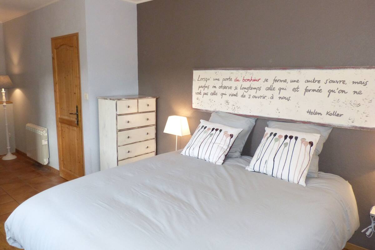 A bedroom with a bed, a dresser, a lamp, and a wall with a quote.