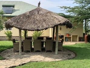 An outdoor dining area with a thatched roof, wicker chairs, and a stone-paved patio. - Ol Bobongi House (Nanyuki)