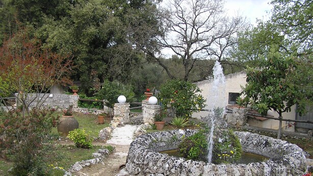 A garden with a fountain, stone walls, and potted plants. - The farther you are from the world, the more beautiful the world seems (Noto (SR))