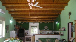 A cozy kitchen with a wooden ceiling, a dining area with a table set for four, and a green sofa. - The farther you are from the world, the more beautiful the world seems (Noto (SR))