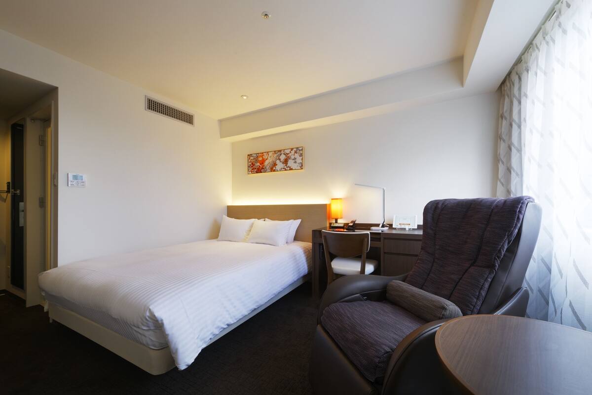 Ein Hotelzimmer mit einem Einzelbett, einem Schreibtisch mit Stuhl und einem kleinen Tisch.