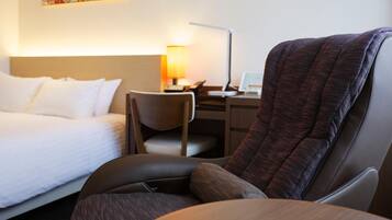 Una habitación de hotel con una cama, un escritorio con lámpara, una silla y un sillón grande.
