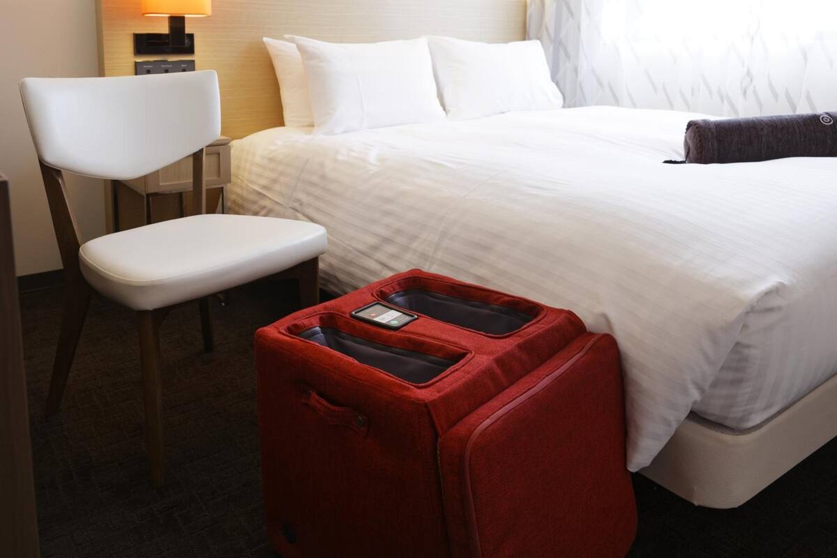 Ein Hotelzimmer mit einem Bett, einem Sessel und einem roten Koffer.
