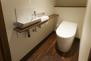 Un baño moderno con un lavamanos blanco, un inodoro y una estantería de madera.