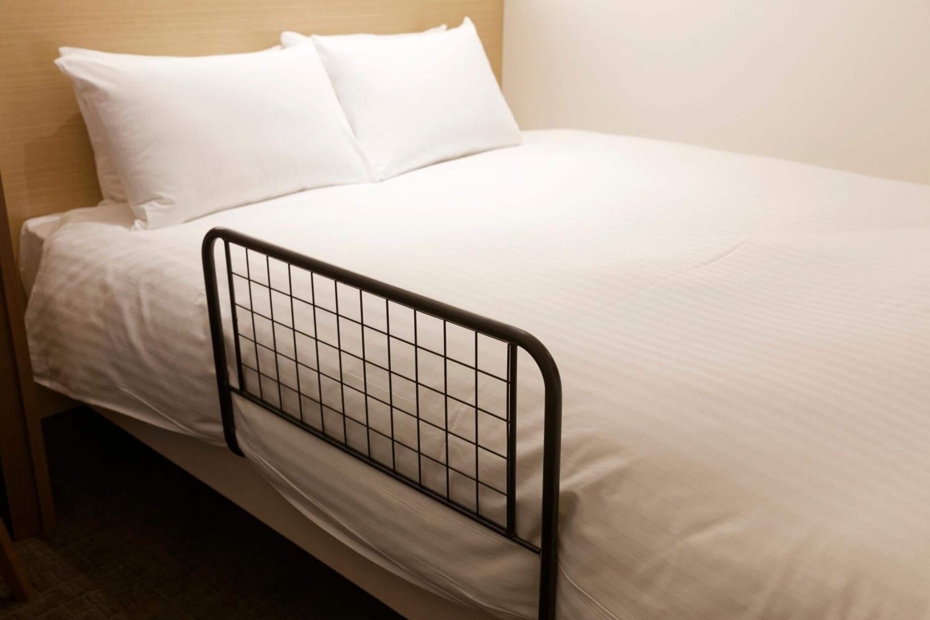 A single bed with a metal headboard, white bedding, and a wooden headboard panel.