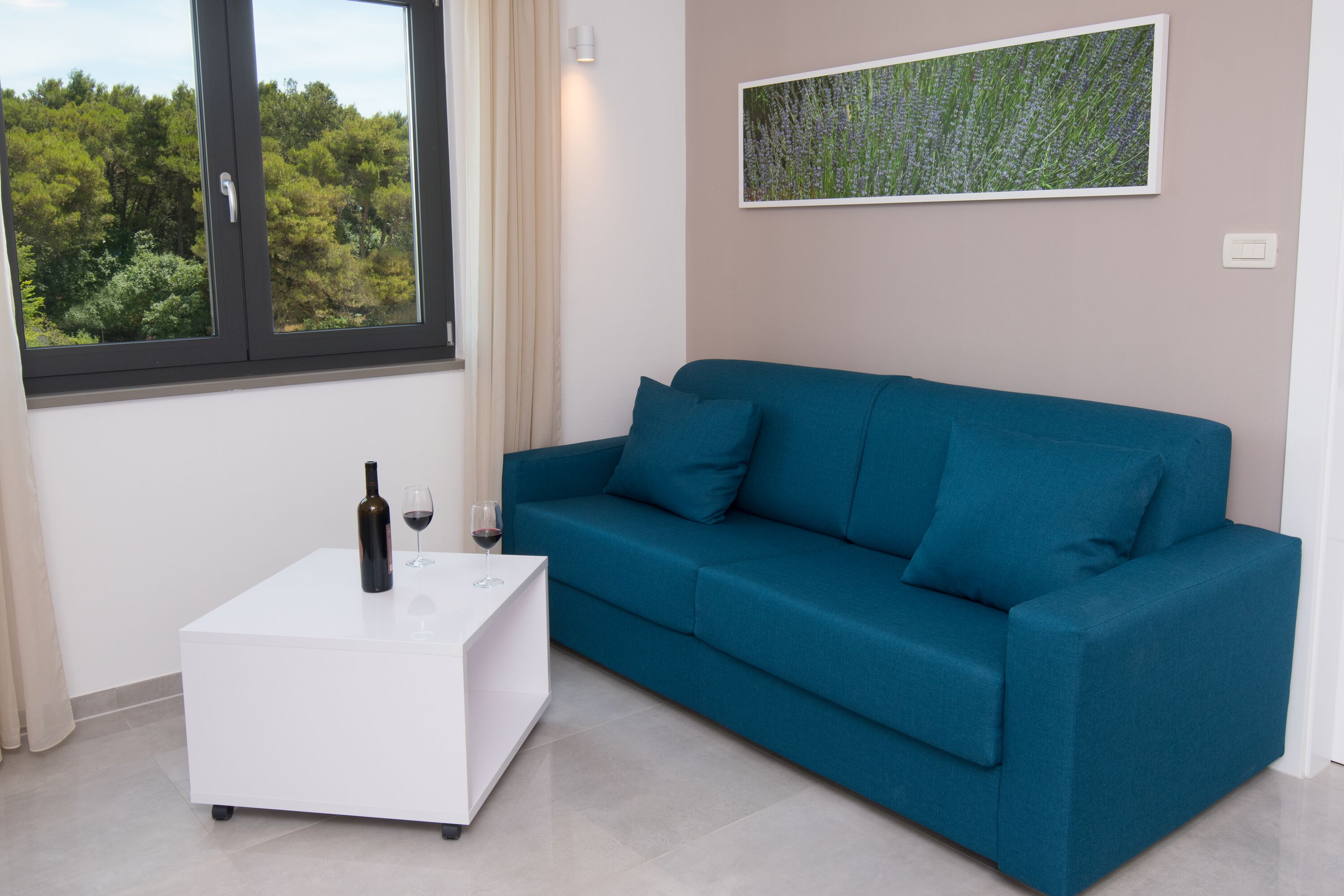 A modern living room with a teal sofa, a white coffee table, and a wine bottle.