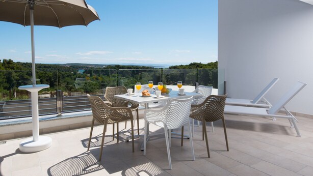 Una terraza con una mesa lista para el desayuno, que incluye zumo de naranja y croissants, con vistas a un paisaje pintoresco.