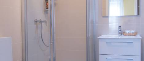 A modern bathroom with a glass-enclosed shower, a white toilet, and a vanity with a mirror.