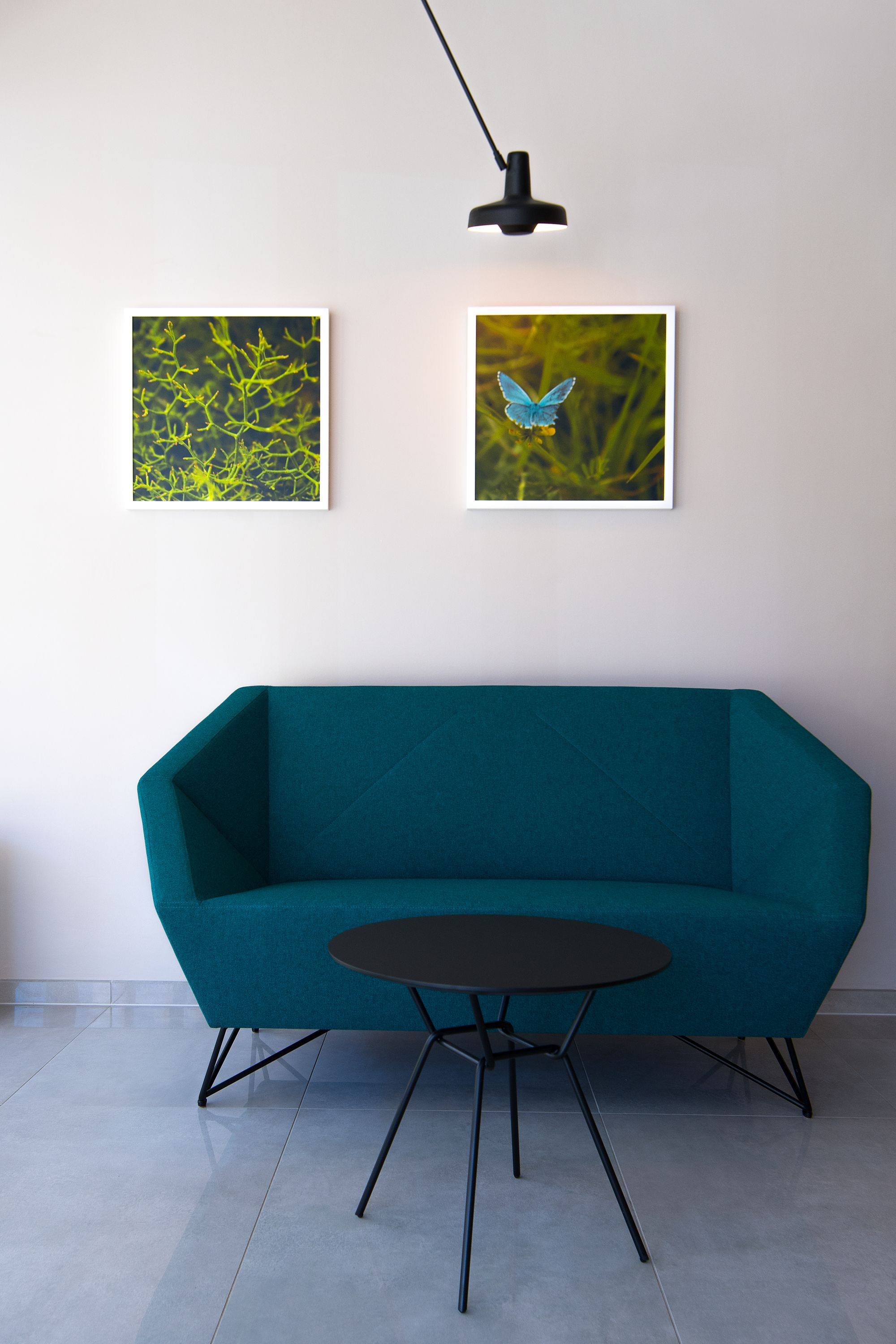 Un sofà blau mar amb una taula de cafè negra al davant, dos quadres al mur i una làmpada de terra negra.