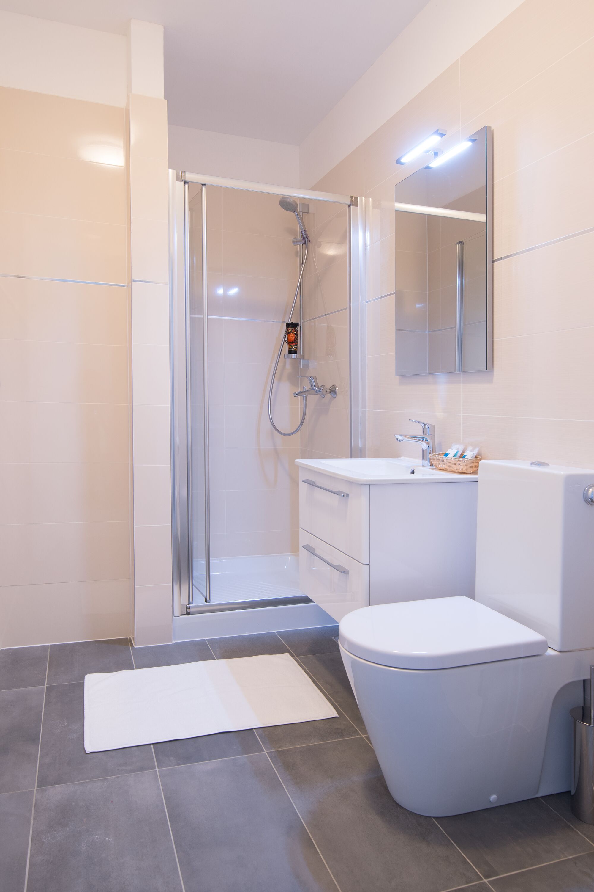Een moderne badkamer met een douchecabine van glas, een wit wastafeltje en een toilet.